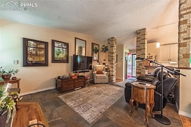 Living area featuring decorative columns, lofted ceiling, and stone tile flooring
