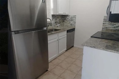 Kitchen featuring appliances with stainless steel finishes, white cabinetry, backsplash, light stone countertops, and light tile patterned flooring