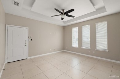 Empty room with light tile patterned flooring, a ceiling fan, baseboards, a tray ceiling, and visible vents
