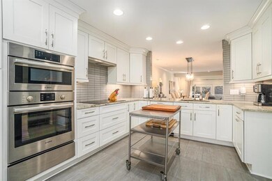 At the heart of the home is the Spacious Chef's Kitchen, featuring Crisp White Custom Cabinetry extending to the ceiling, Stone Countertops, Top-Of-The-Line Stainless Steel Appliances, and a Stunning Muted Gray Subway Tile Backsplash.