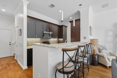 Kitchen with crown molding, a kitchen bar, light wood finished floors, light stone counters, and decorative backsplash