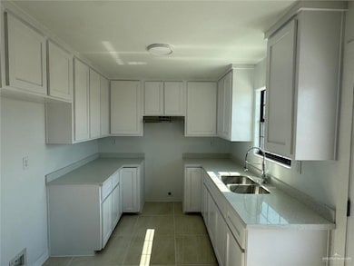 Kitchen featuring white cabinetry, light tile patterned floors, light stone countertops, and under cabinet range hood