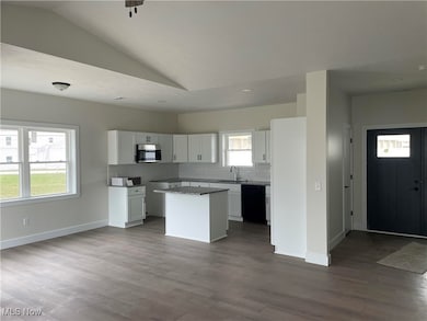 Kitchen with tasteful backsplash, a kitchen island, open floor plan, lofted ceiling, and white cabinetry