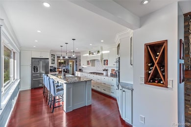 Kitchen with hanging light fixtures, a kitchen breakfast bar, glass insert cabinets, light stone countertops, and built-in stainless steel appliances