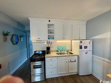 Kitchen with under cabinet range hood, stainless steel gas range oven, freestanding refrigerator, white cabinetry, and a wainscoted wall