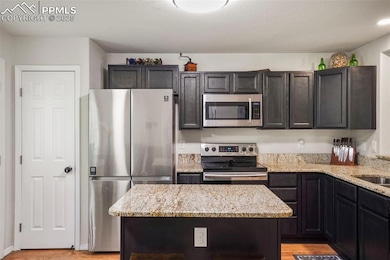 Kitchen with stainless steel appliances, light stone counters, light wood-style flooring, and a center island