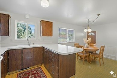 Kitchen with a peninsula, light countertops, decorative light fixtures, and dark brown cabinets