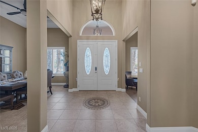 Foyer entrance with light tile patterned floors, baseboards, a high ceiling, and ceiling fan with notable chandelier