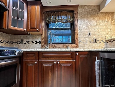 Kitchen with glass insert cabinets, stainless steel stove, wine cooler, tasteful backsplash, and granite countertop.
