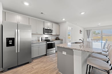 Kitchen featuring appliances with stainless steel finishes, light stone counters, light wood-style floors, recessed lighting, and a kitchen bar
