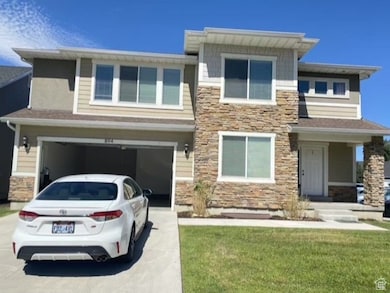 View of front of property with stone siding, concrete driveway, a front yard, and a garage