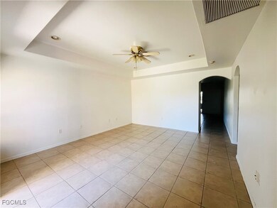 Empty room featuring a raised ceiling, arched walkways, light tile patterned flooring, and ceiling fan