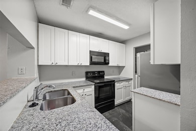 Kitchen featuring black appliances, white cabinets, light stone counters, a textured ceiling, and dark wood finished floors