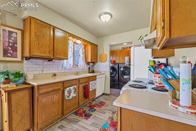 Kitchen featuring washer and dryer, a sink, light countertops, white appliances, and brown cabinetry