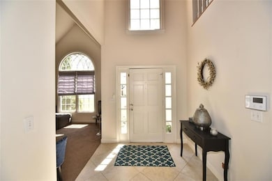 Foyer with a towering ceiling, light tile patterned floors, and light carpet