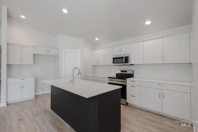 Kitchen featuring stainless steel appliances, white cabinets, light wood-type flooring, a center island with sink, and dark cabinetry