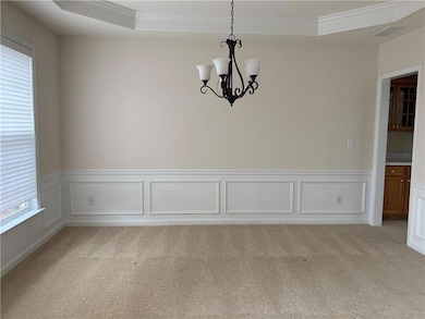Unfurnished dining area featuring a chandelier, light colored carpet, crown molding, wainscoting, and a decorative wall