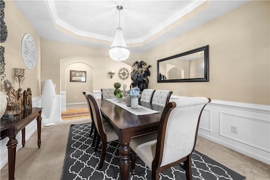 Dining area featuring carpet flooring, a decorative wall, ornamental molding, wainscoting, and a chandelier