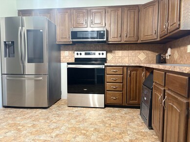 Kitchen with appliances with stainless steel finishes, light countertops, backsplash, and stone finish floors