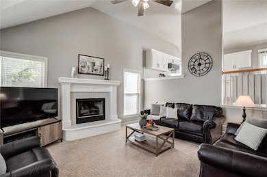 Living room with vaulted ceiling, light colored carpet, a fireplace, and ceiling fan