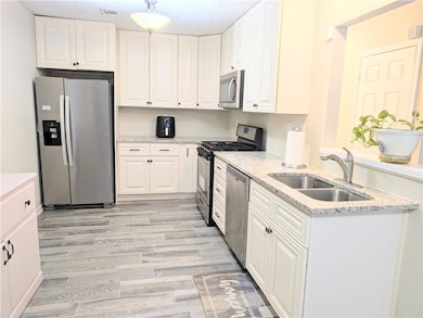 Kitchen featuring appliances with stainless steel finishes, white cabinetry, and light stone countertops