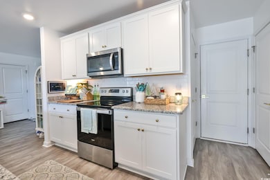 Kitchen with stainless steel appliances, decorative backsplash, white cabinetry, light stone counters, and light wood-type flooring