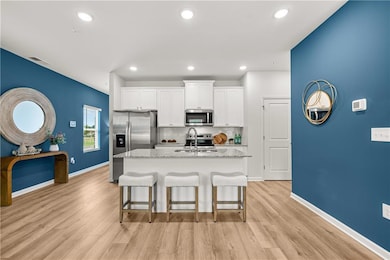 Kitchen with white cabinets, stainless steel appliances, decorative backsplash, a breakfast bar, and light stone counters