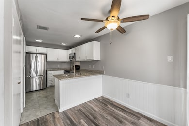 Kitchen featuring appliances with stainless steel finishes, a peninsula, ceiling fan, a wainscoted wall, and dark wood-style flooring