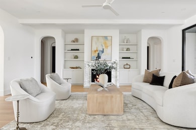 Living room featuring arched walkways, a fireplace, light wood-style flooring, ceiling fan, and beam ceiling