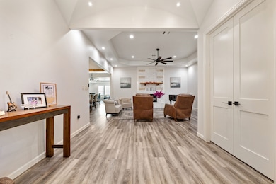 Living area with a large fireplace, light wood-style flooring, a ceiling fan, recessed lighting, and a raised ceiling