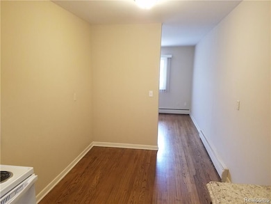 Empty room with a baseboard radiator and dark wood-style flooring