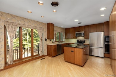 Kitchen with wallpapered walls, stainless steel appliances, recessed lighting, light wood finished floors, and a center island