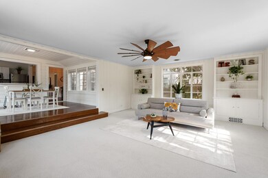 Carpeted living room featuring built in features, healthy amount of natural light, ceiling fan, and wood walls