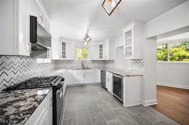 Main kitchen with dark stone countertops, tasteful backsplash, stainless steel appliances, white cabinetry, and glass insert cabinets