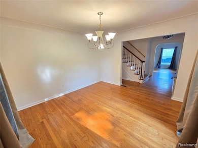 Unfurnished dining area with light wood-style floors, arched walkways, stairs, and a chandelier