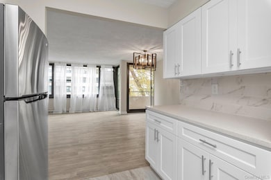 Kitchen with freestanding refrigerator, white cabinetry, decorative backsplash, a chandelier, and light stone countertops