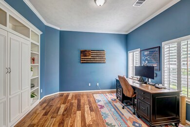Glass french doors reveal a home office with window shutters and custom built-in bookcases.