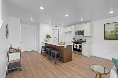 Kitchen featuring a kitchen bar, a peninsula, white cabinets, stainless steel appliances, and light wood-style floors