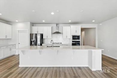 Kitchen with appliances with stainless steel finishes, wall chimney range hood, light wood-type flooring, a large island, and recessed lighting