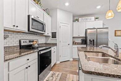 Kitchen featuring appliances with stainless steel finishes, white cabinetry, light wood-style flooring, decorative backsplash, and hanging light fixtures