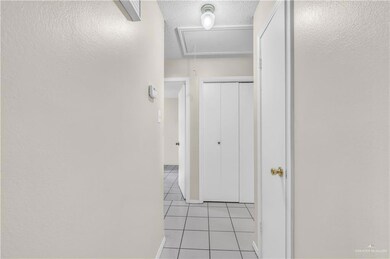 Hall with attic access, light tile patterned flooring, and a textured ceiling
