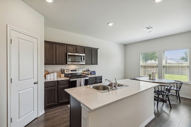 Kitchen with appliances with stainless steel finishes, dark wood-type flooring, light stone countertops, dark brown cabinetry, and recessed lighting