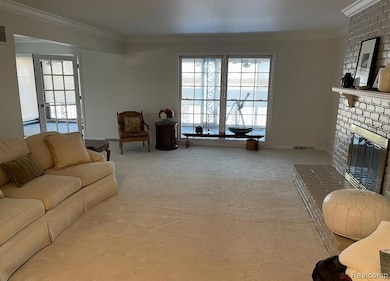 Living room with ornamental molding, light colored carpet, healthy amount of natural light, and a brick fireplace