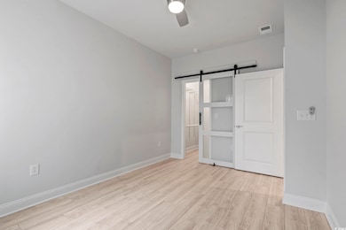 Unfurnished bedroom featuring a barn door, light wood-style floors, a ceiling fan, and connected bathroom