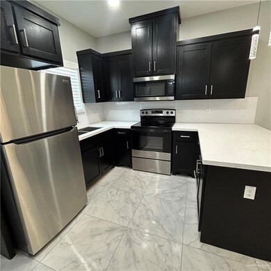 Kitchen with dark cabinets, appliances with stainless steel finishes, light marble finish flooring, backsplash, and recessed lighting