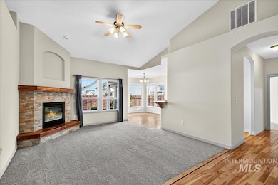 Unfurnished living room featuring a glass covered fireplace, ceiling fan, arched walkways, a chandelier, and a textured ceiling