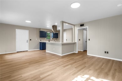 Kitchen featuring wooden walls, blue cabinetry, light countertops, light wood-style flooring, and a peninsula