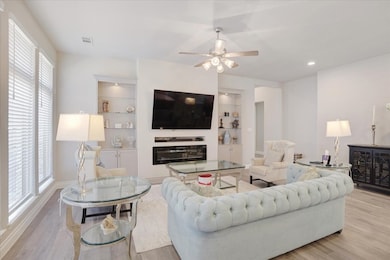 Living area featuring light wood finished floors, built in shelves, and ceiling fan