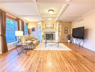 Living room with a high end fireplace, beamed ceiling, light wood-type flooring, and coffered ceiling