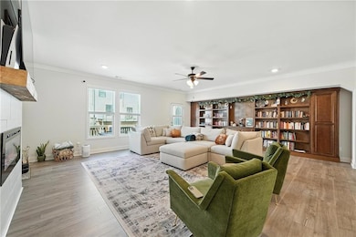 Living area with a tiled fireplace, ceiling fan, ornamental molding, light wood finished floors, and recessed lighting and custom built wall unit